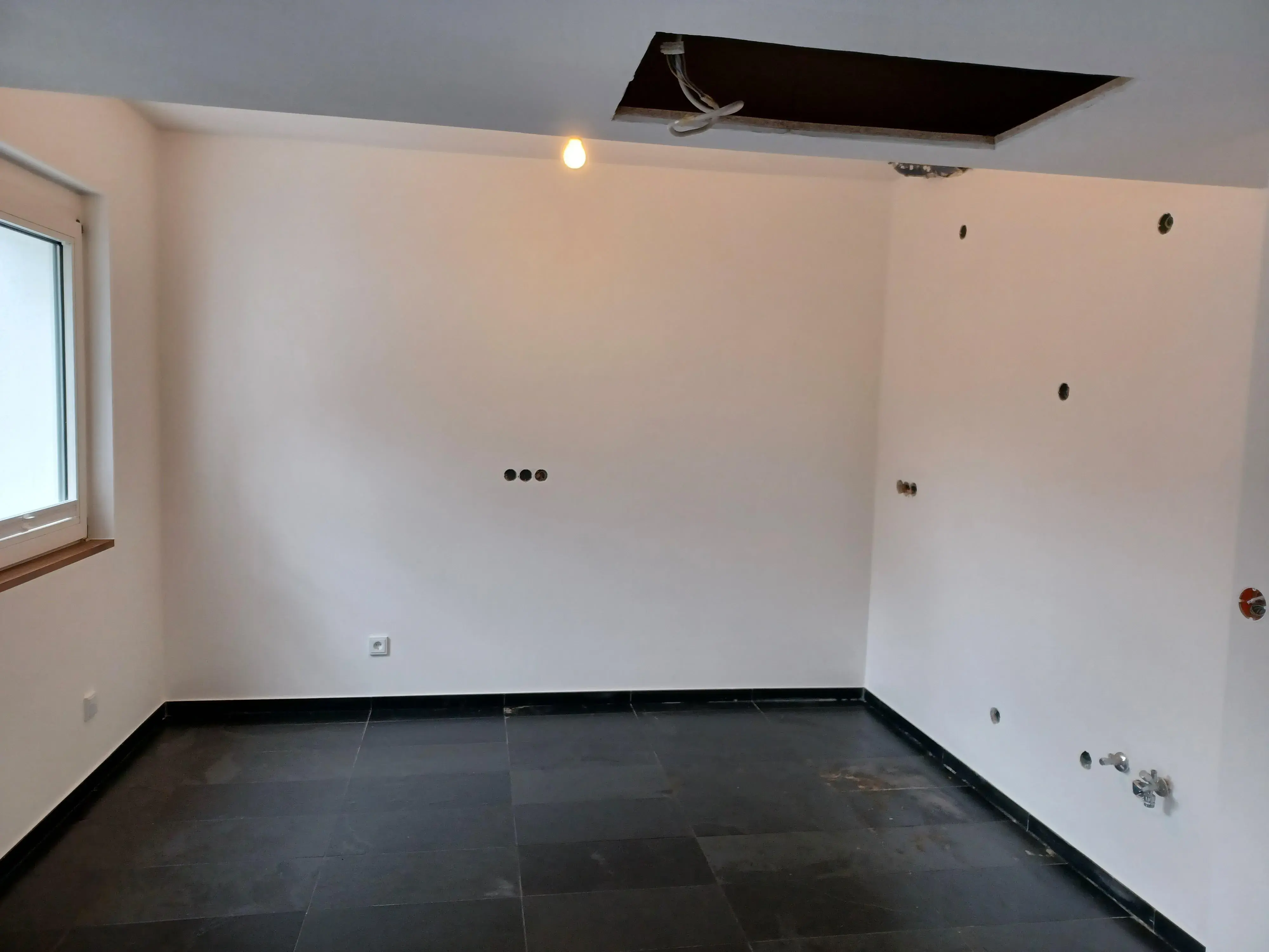 Leerer Raum mit weißen Wänden, schwarzen Fliesen und Loch in der Decke.