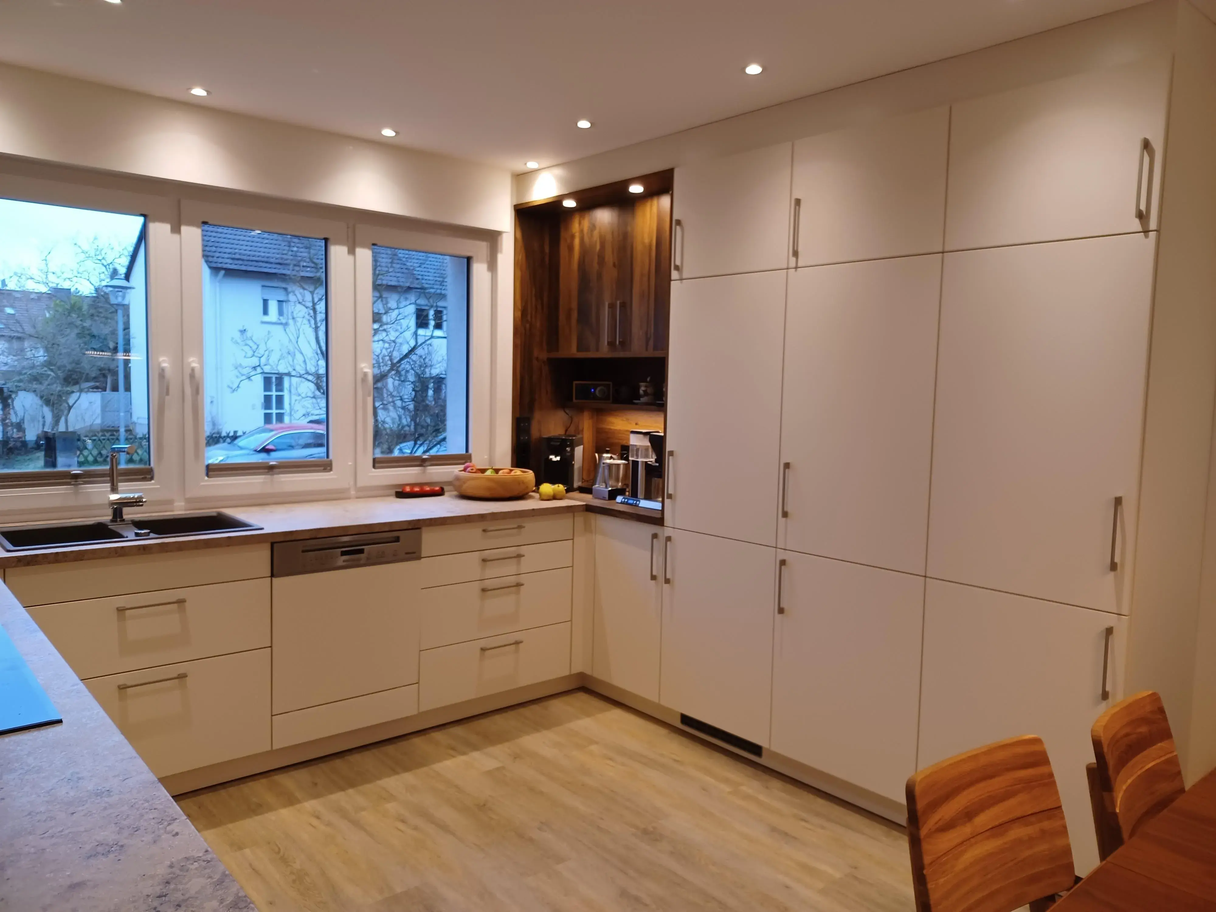 Moderne, helle Küche mit weißen Schränken, Holzdetails und großem Fenster.
