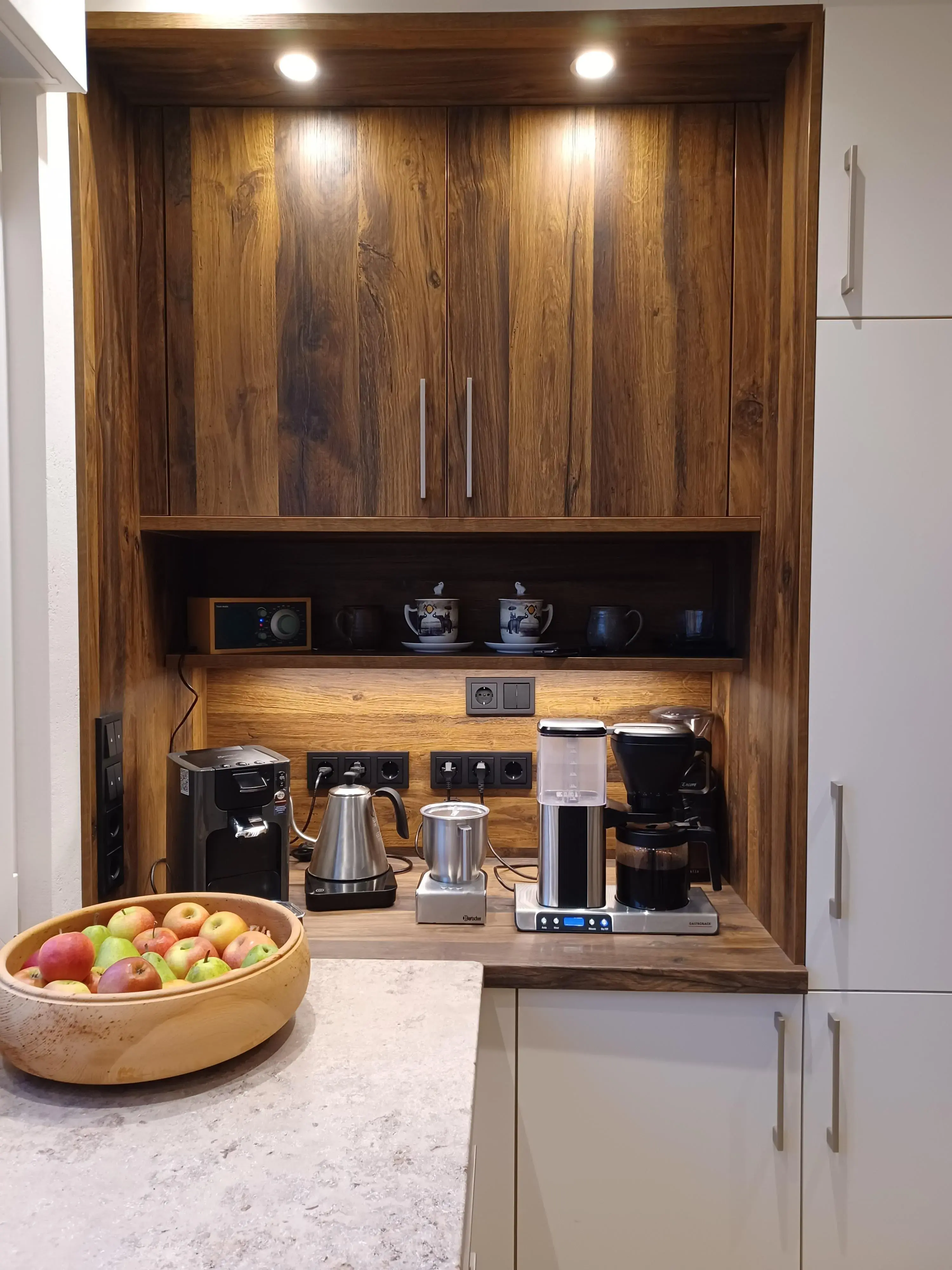 Moderne Kaffeeecke mit verschiedenen Kaffeemaschinen, Tassen und einer Schale Äpfel.