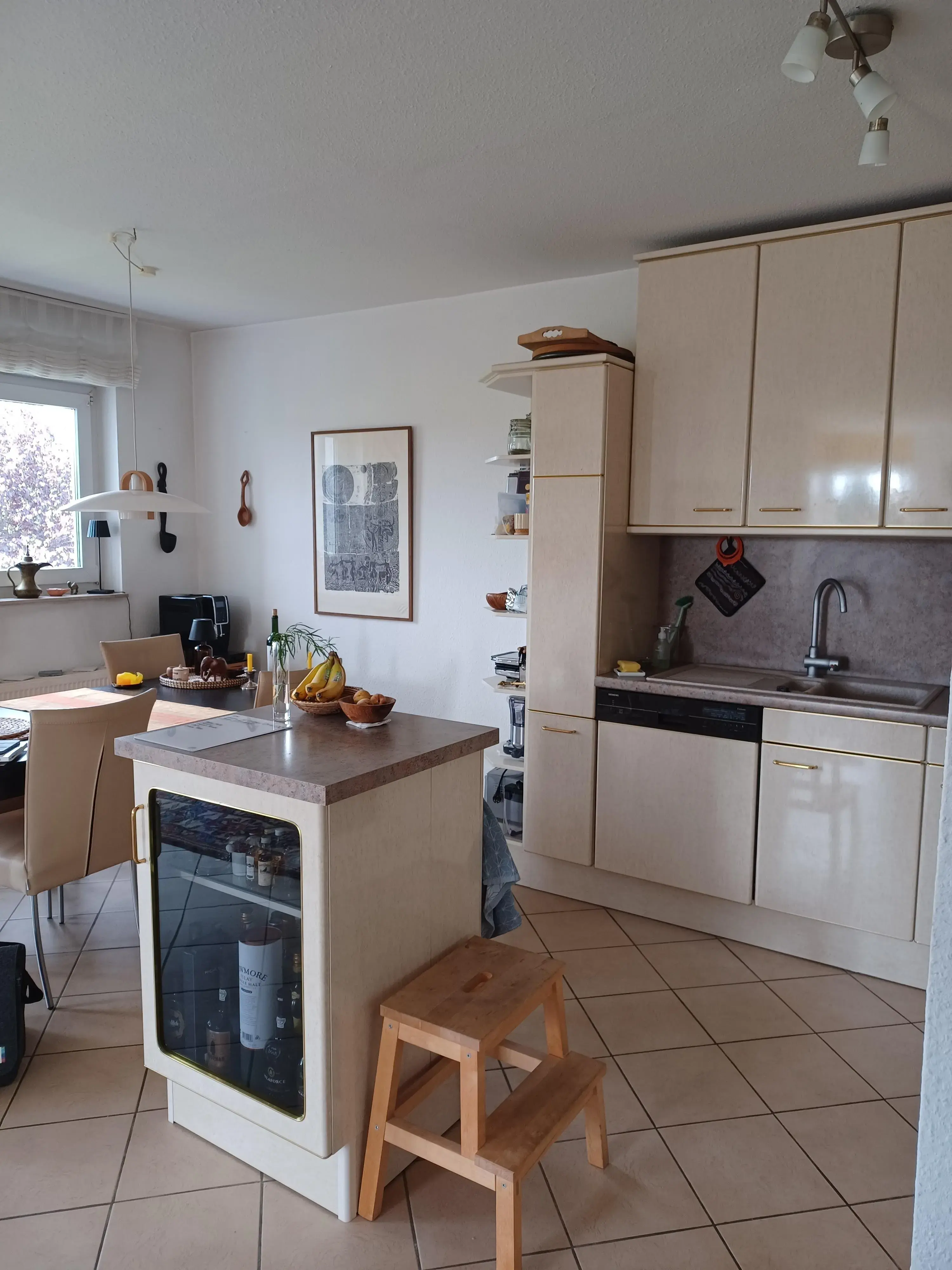 Helle Küche mit Essbereich, Obstschale auf der Theke, Holztritt und Fenster.