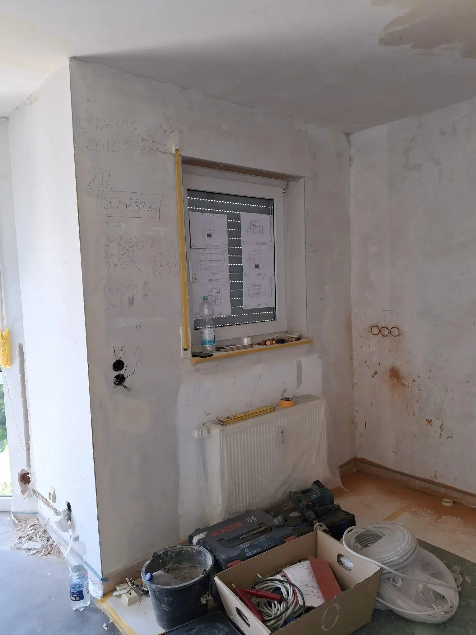 Renovierungsraum mit Kartons, Malerutensilien und einem Fenster mit Folie abgedeckt.