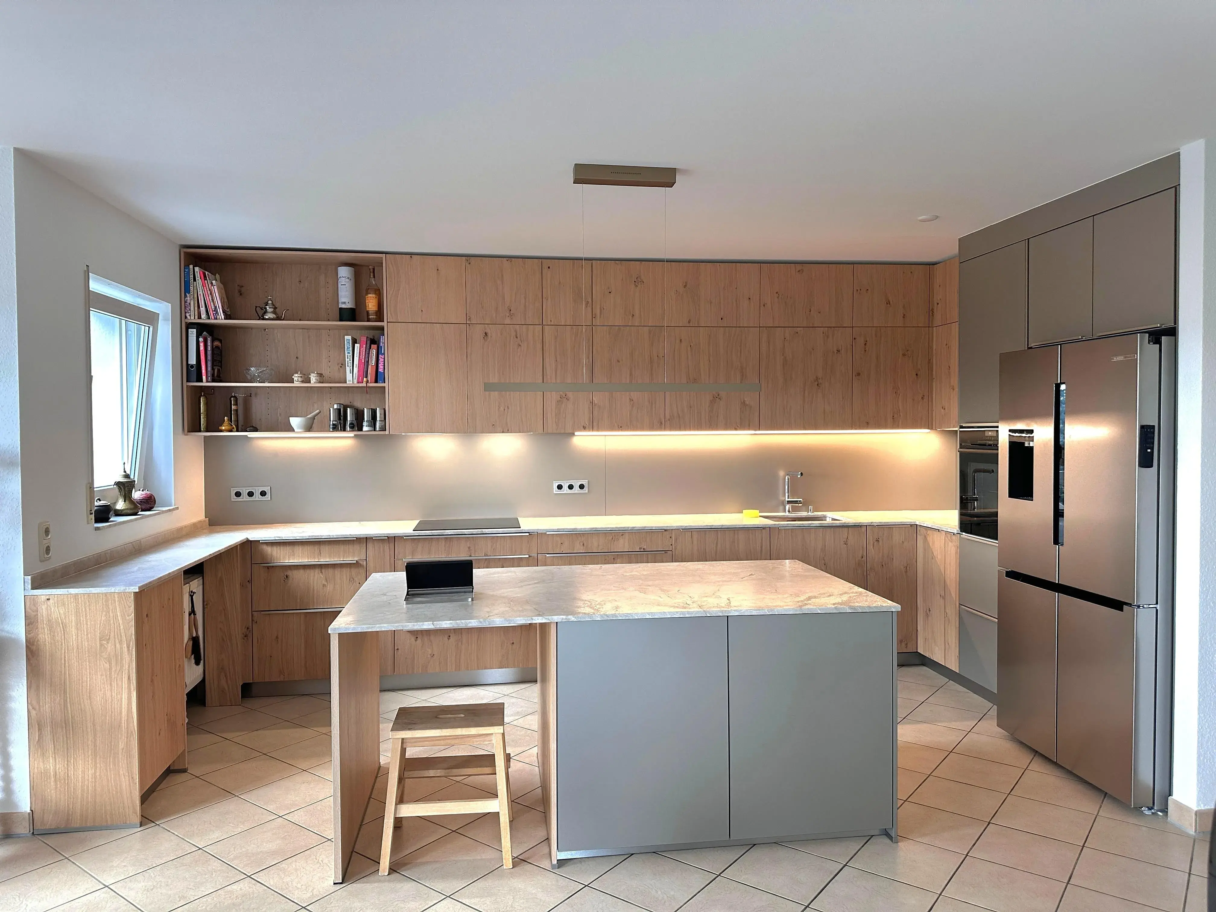 Moderne Küche mit Holzfronten, Kücheninsel, Stuhl und Edelstahlkühlschrank.