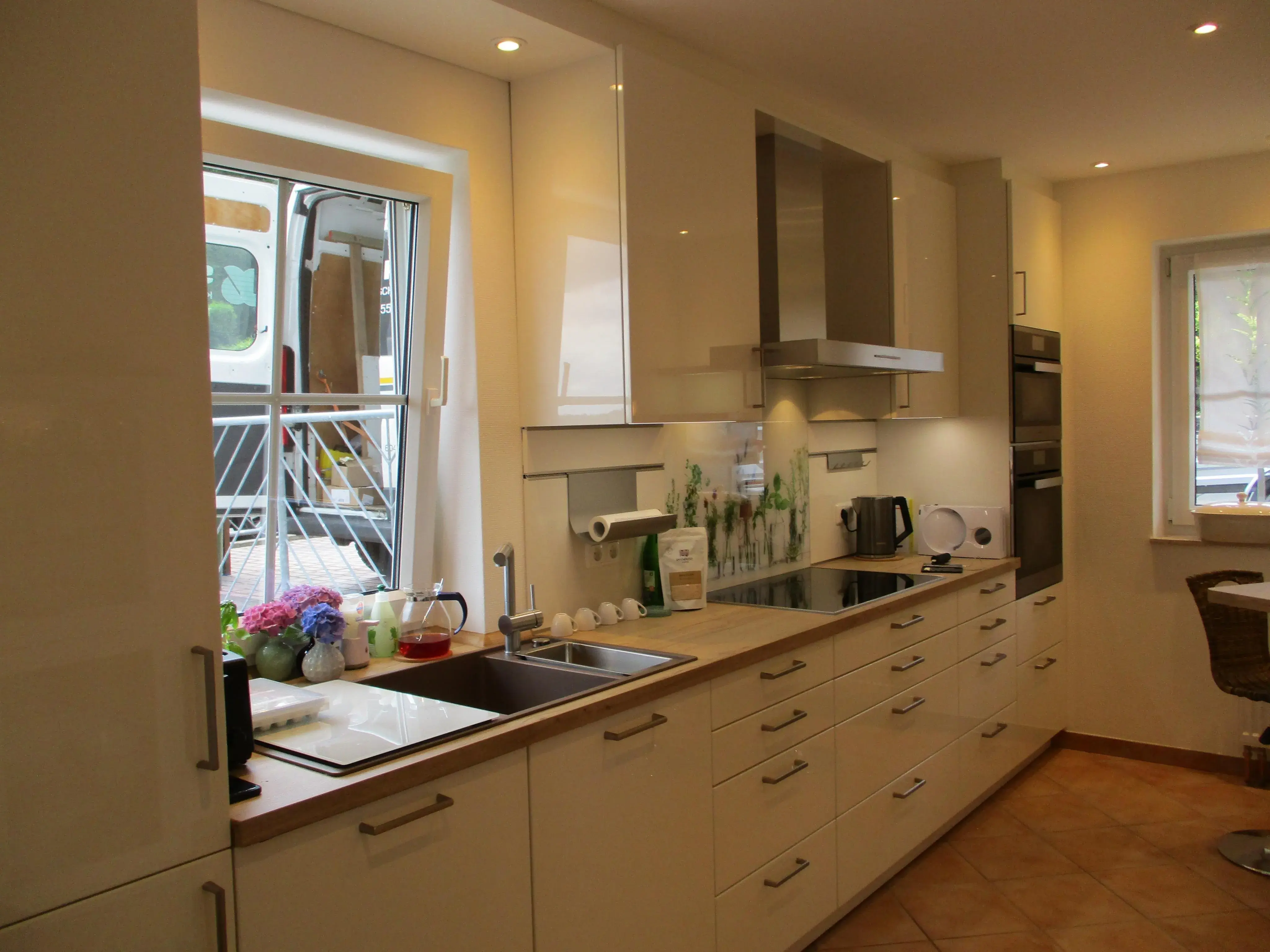 Moderne Küche mit weißen Schränken, großem Fenster und Elektrogeräten.
