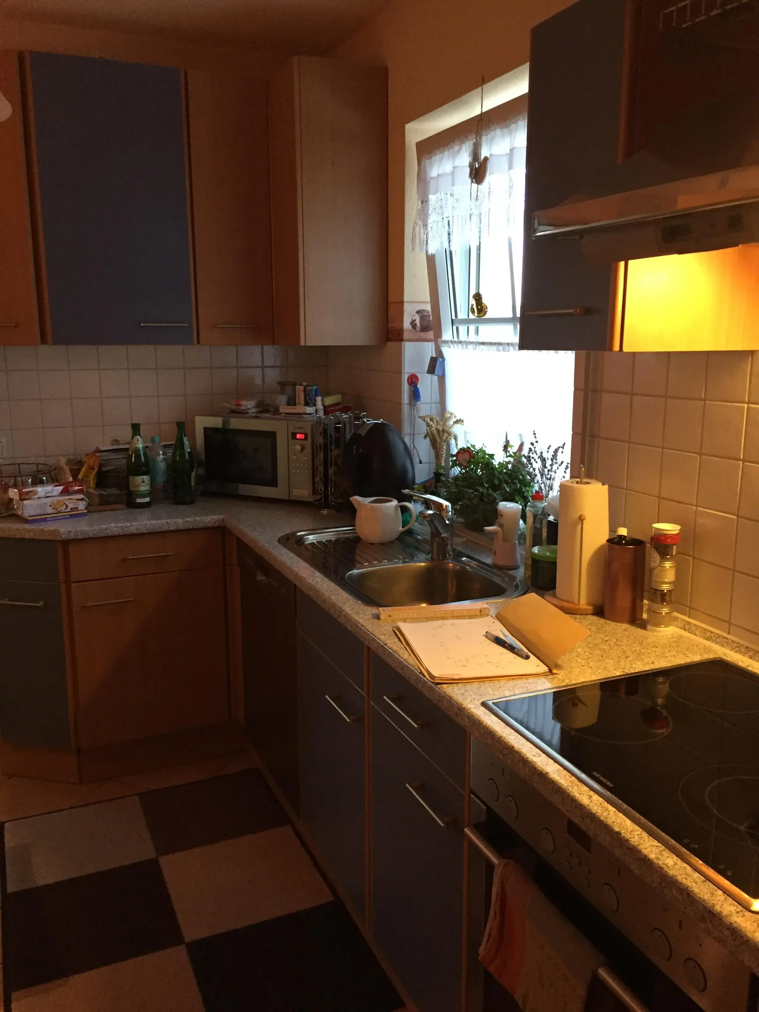 Gemütliche Küche mit Herd, Spüle und Arbeitsflächen, Tageslicht kommt durchs Fenster.