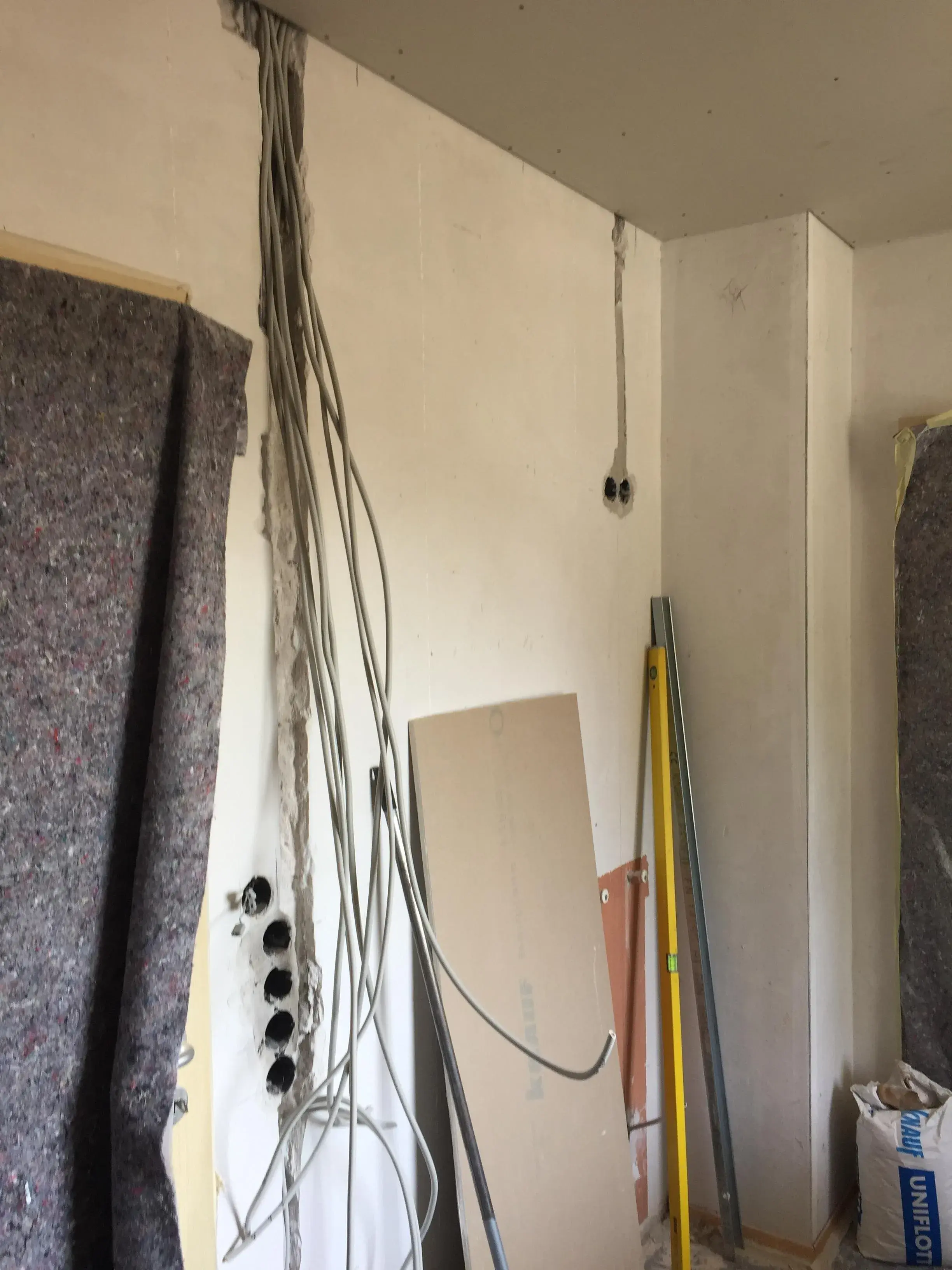 Kabel hängen an einer weißen Wand in einem renovierten Raum, Leiter und Baumaterial stehen daneben.