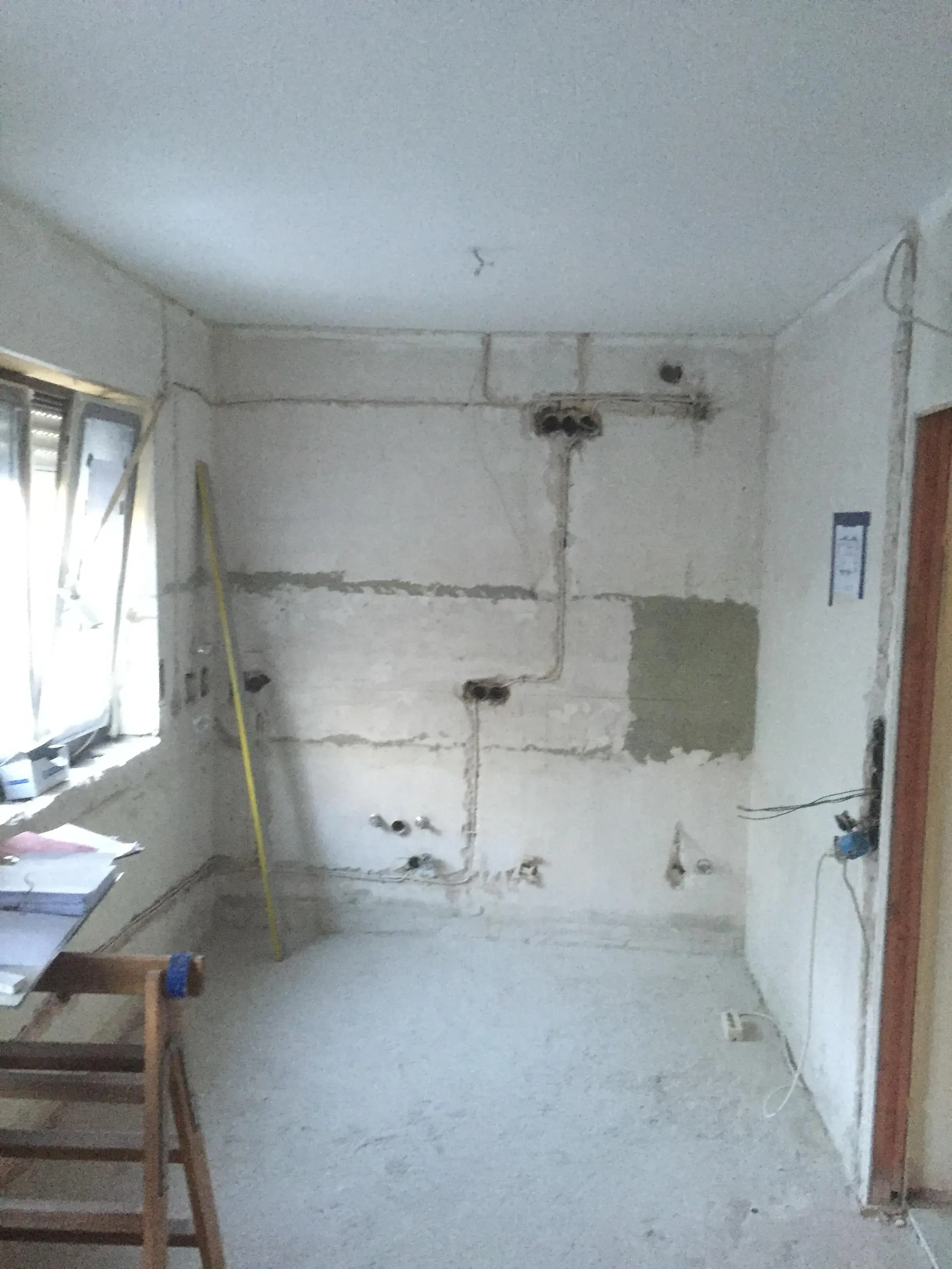 Leerer Raum mit renovierungsbedürftigen Wänden, Fenster links, Zollstock an der Wand.