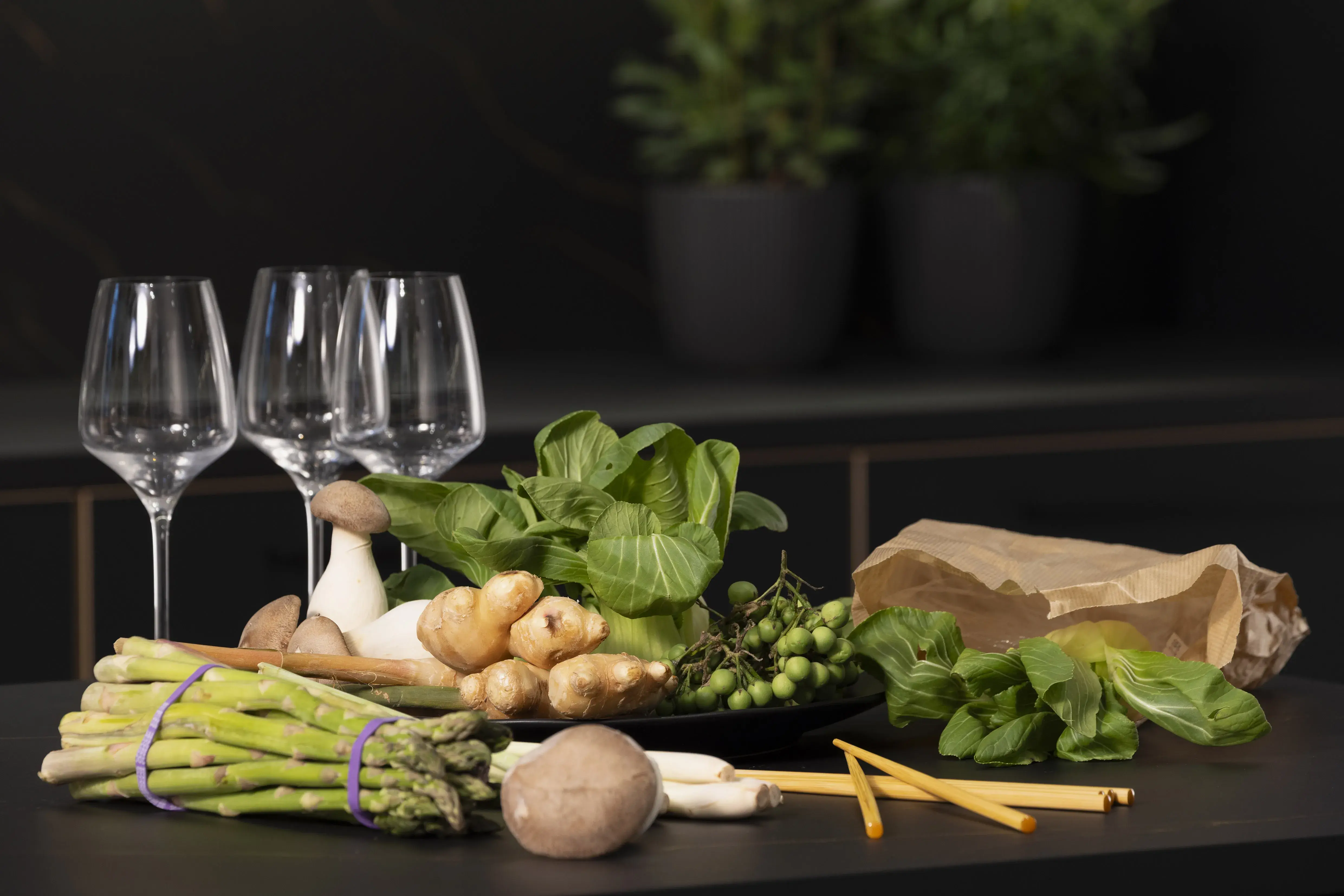 Gemüse, Spargel, Pilze und Spinat neben drei Weingläsern auf dunklem Tisch.