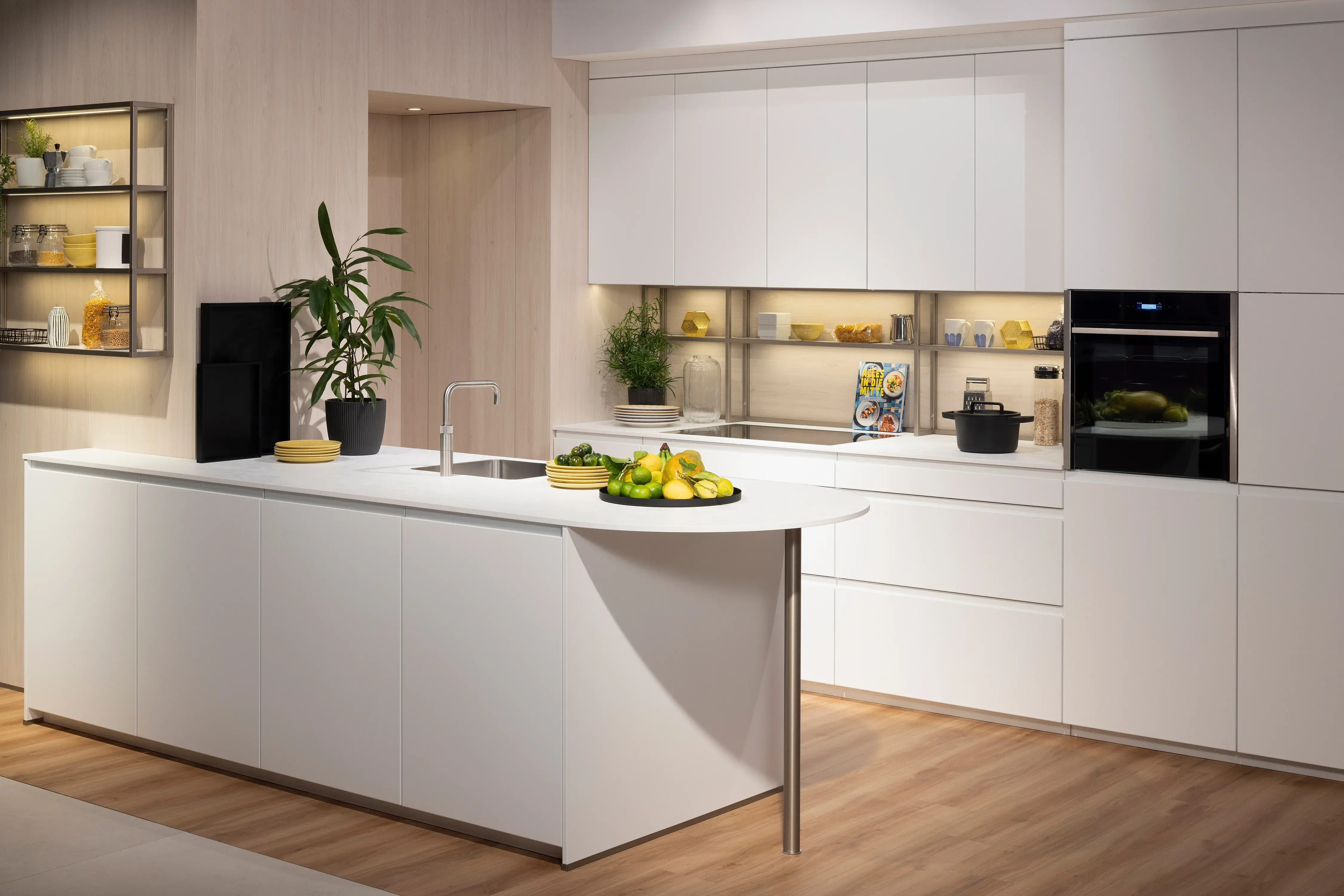 Moderne weiße Küche mit Kücheninsel, Pflanzen und frischem Obst auf der Arbeitsfläche.